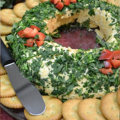 A Rada Party Spreader next to a Christmas themed cheese wreath with sliced strawberries on top and surrounded by circle crackers