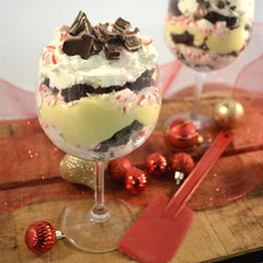 A peppermint dessert with a layer of pudding, fudge and peppermint layered in a wine glass with chocolate shavings for its topping next to a red Rada Mixing Spatula