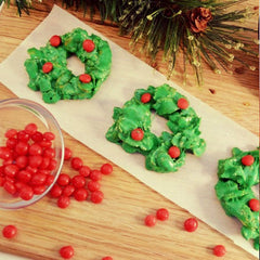 Christmas wreath cookies with red hot candies in green frosting on a strip of opaque parchment paper