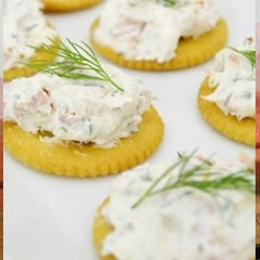 Circular butter crackers with Smoked Salmon Spread on top of each cracker with a small sprig of garnish