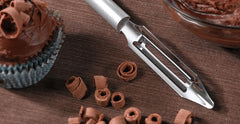 A RADA stainless steel Vegetable Peeler with a silver brushed aluminum handle next to chocolate shavings and a double chocolate muffin with a chocolate shaving topping