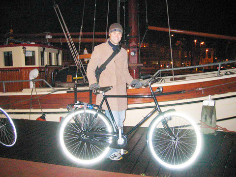 Image of a young man (Eric Jacoby) standing with a black bicycle in front of a sailboat at night 