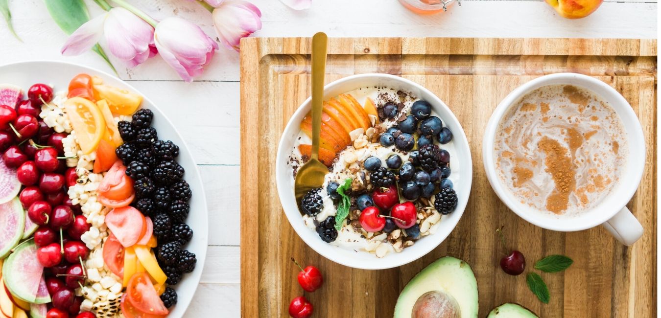 Bird's eye view of a white wooden table with a fruit tray, coffee, and greek yogurt