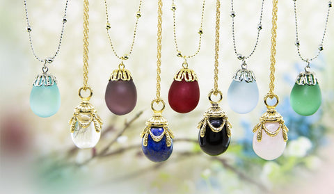 Elegant glass egg-shaped pendants on gold chains each with unique gemstones in various colors