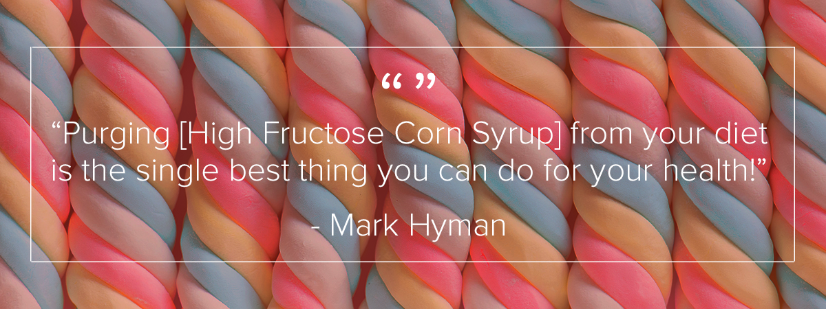 9 twisting sugar candies are arranged in a line going left to right. The candies are standing vertical. There are three strands of candy twisting to make each candy. The colors of the twists alternate between white, pink, blue, and yellow. Above the image is a quote by Mark Hyman which reads: "Purging [High Fructose Corn Syrup] from your diet is the single best thing you can do for your health."