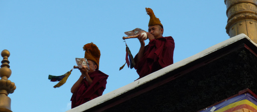 Buddhist monks blowing horns in India on a clear blue day.