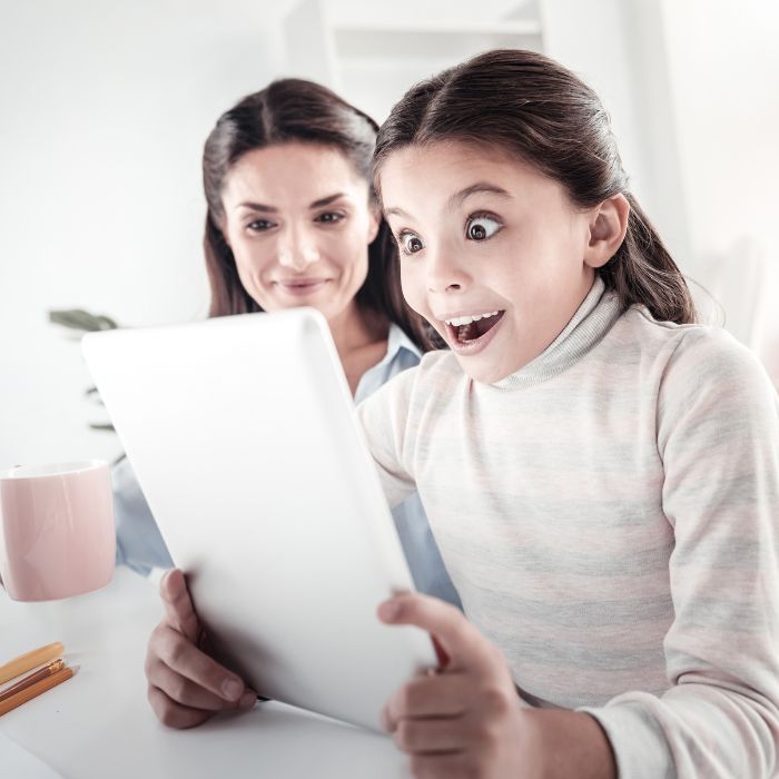A SURPRISED CHILD WITH HER MOTHER LOOKING AT TABLET