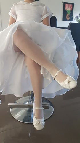 Girls legs showing from under her Frist Communion dress wearing white mesh tights.