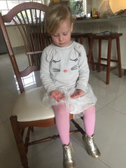 Little girl sitting perched on a chair in a white tutu and pink stockings.