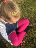 Little blonde girl sitting on the grass with her legs crossed in bright pink tights.