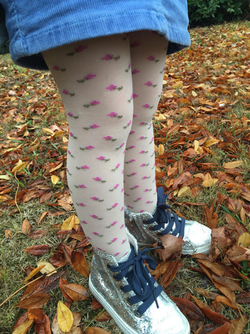 Little girl's legs wearing sneakers and cream tights with tiny pink flowers.