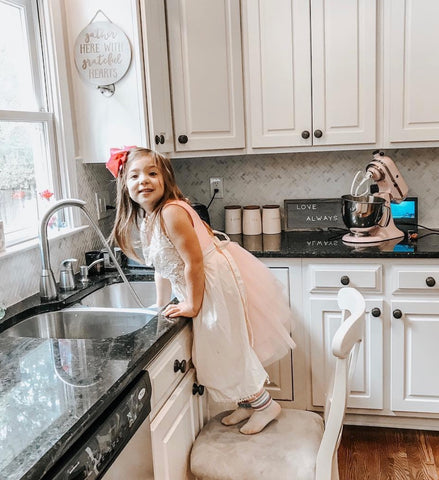 child in farmhouse kitchen wearing apron baking cookies with mom