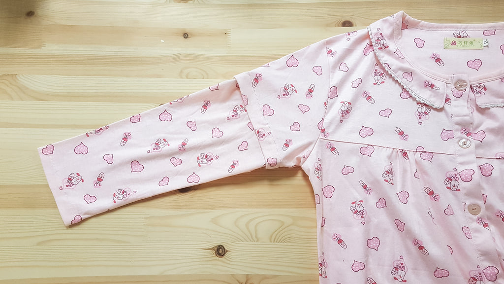 Partial view of pink pyjama top with pink hearts and cartoon dog prints. It is laid on a flat wooden surface and the main focus is the detachable long sleeves.