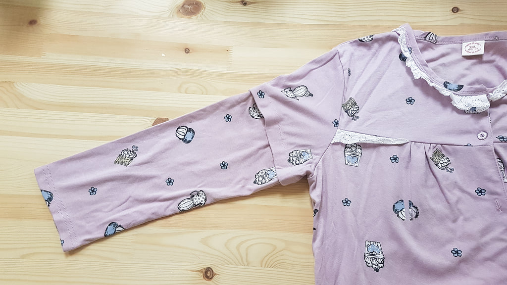 Partial view of a purple pyjama top with various succulent prints. It is laid on a flat wooden surface and the main focus is the detachable long sleeves.