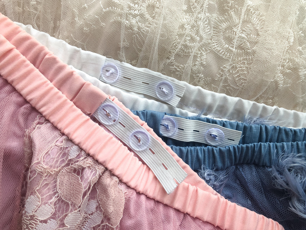 Pink, blue and cream coloured skirts layered on top of each other with adjustable button and elastic exposed.