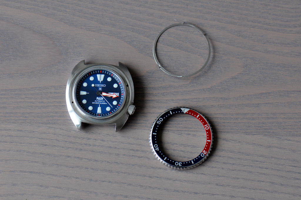 The three components on the table - watch case, bezel, and spring