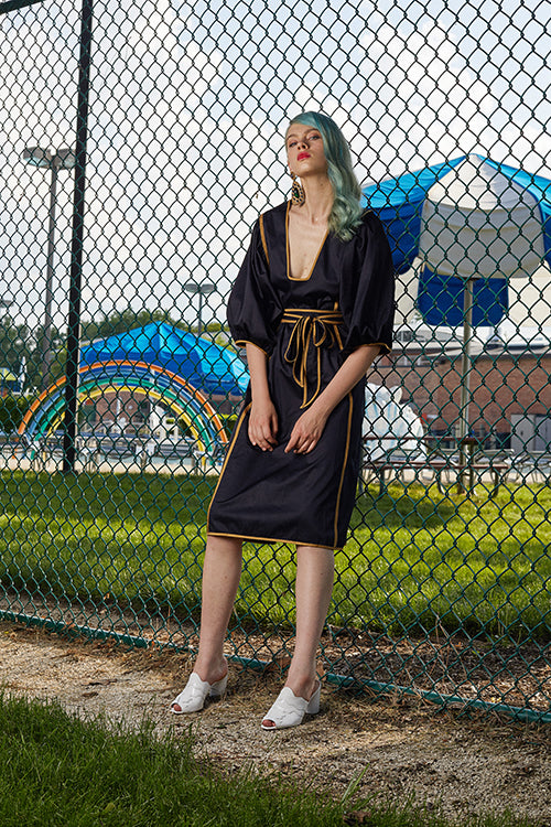 Cynthia Rowley 2019 Resort Collection features a belted mid-length black dress with gold stripes along the sides.