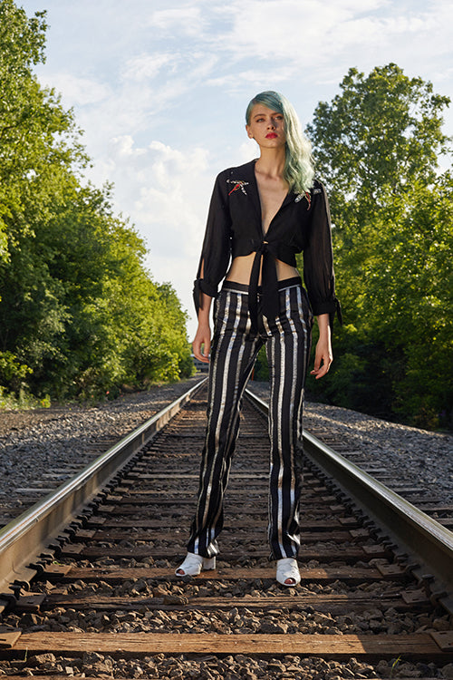 Cynthia Rowley 2019 Resort Collection features a cropped black top tied in front matched with black and silver metallic pinstriped pants. 