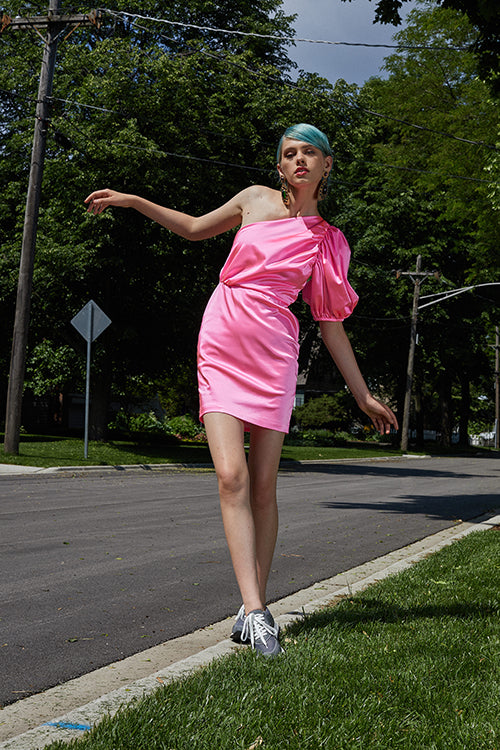 Cynthia Rowley Resort 2019 Collection features a pink silk dress with gathering along one side, paired with grey sneakers and large gold earrings. 