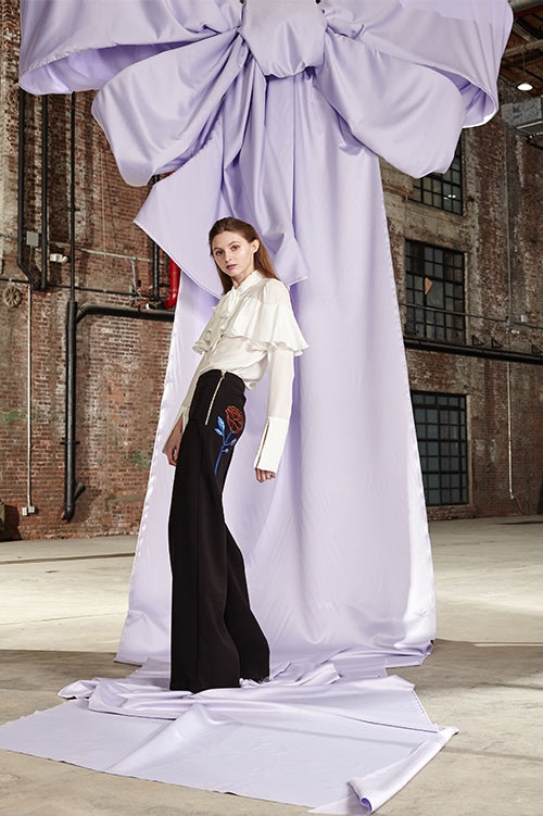 Cynthia Rowley Fall 2017 Look 20 featuring a white silk chiffon blouse with ruffle across chest and neck tie and wool crepe flare pants with a leather appliqué rose on the back