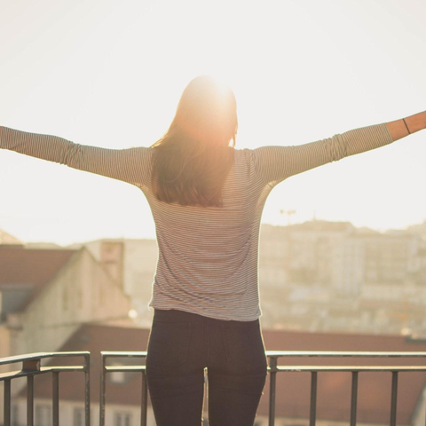 woman standing in morning sunshine with outstretched arms