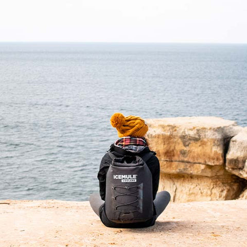 A hiker wears her IceMule cooler overlooking the ocean from a beachside cliff. 