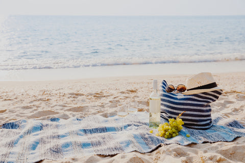 A shot of a beach blanket with a beach bag and miscellaneous items spread about.