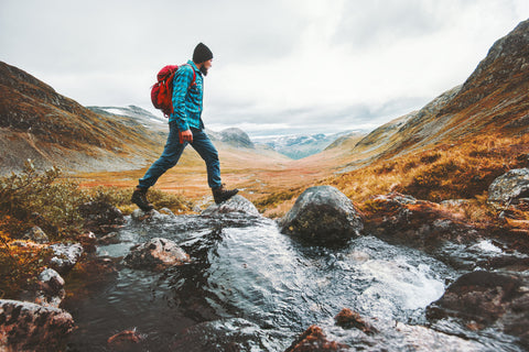 A hiker make his way across a small stream in the mountains of Scandinavia.