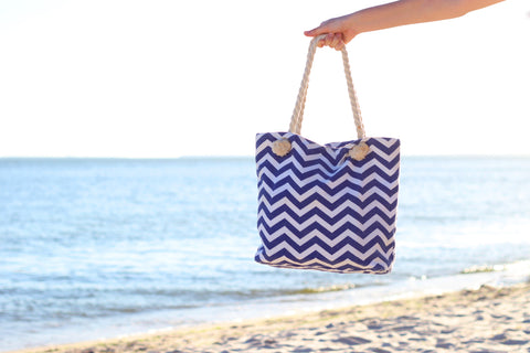A tote bag held by a woman's hand with the ocean in the background.