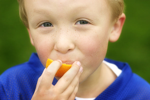 Young boy in soccer jersey eating oranges