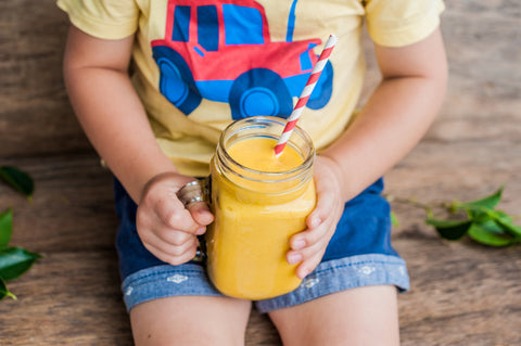 A kid drinks fresh orange juice out of a mason jar. 