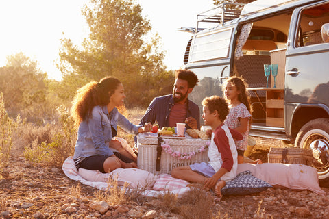 A family on vacation gathers around a picnic basket for a meal.