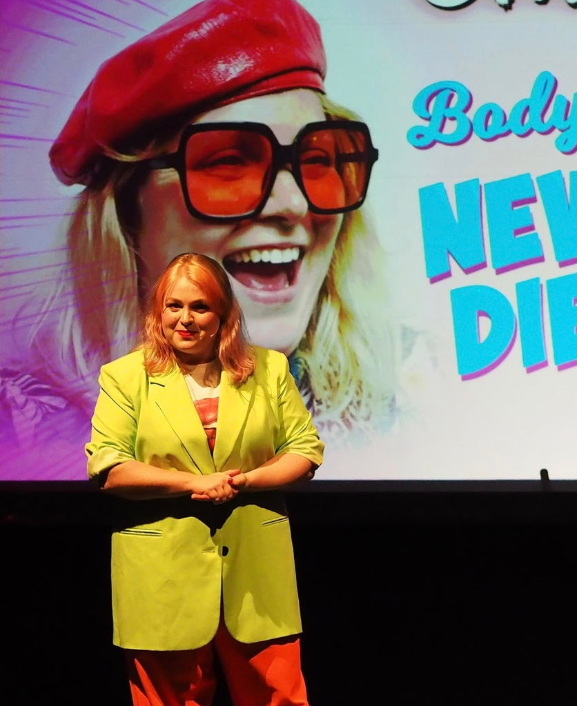 Joeley speaks on stage in front of a poster of herself