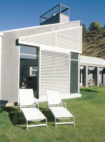 modern home with white sun shutters and two recliner outdoor chairs