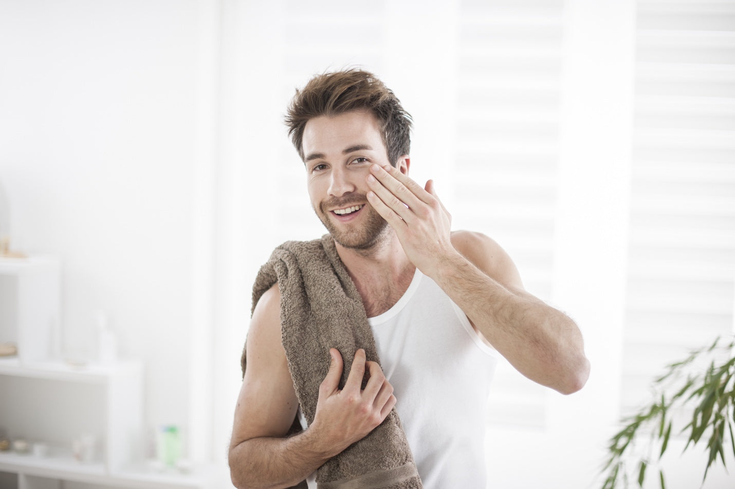 Happy man holding a towel applying face moisturizer