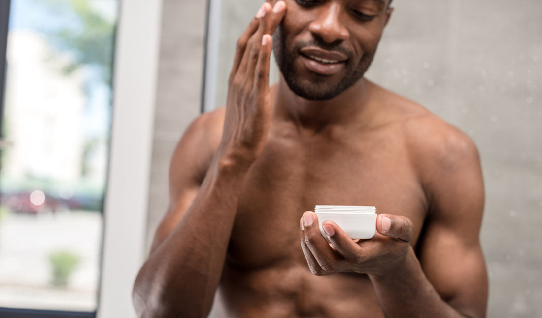 shirtless black man applying facial cream