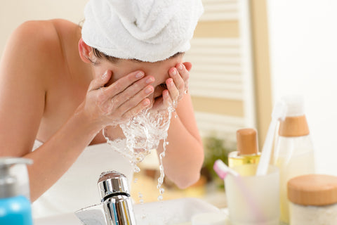 woman splashing face with water in bathroom sink