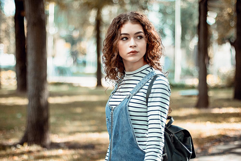 Woman in denim jumpsuit carrying a vintage leather backpack