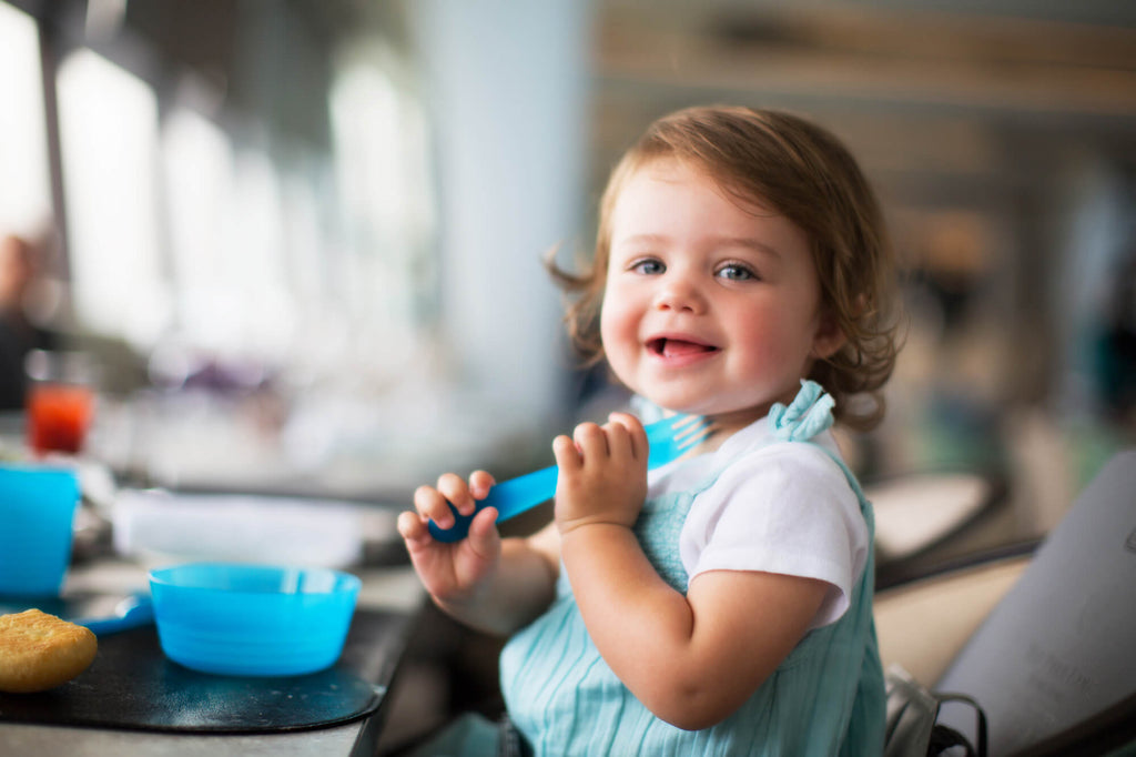 2 years old baby, sitting on a Bombol Foldable Booster Seat in a restaurant, playing with a plastic fork