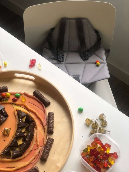 Halloween candies arranged in a tray with Pop-Up booster on a chair next to it.