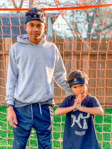 Two young boys standing in front of a soccer net wearing  protective headwear - 2nd Skull Headband