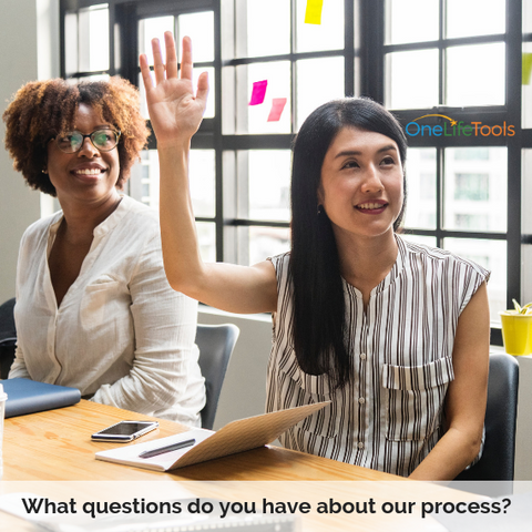 Two women seated in office One with hand raised to ask a question