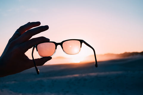 man holding sunglasses up to sunset to look at the tint of the lens