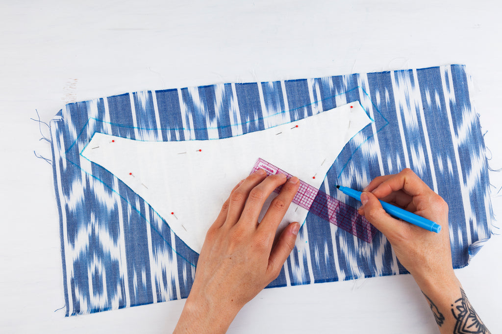 white sleeve pattern piece pinned onto blue patterned fabric, hands tracing around