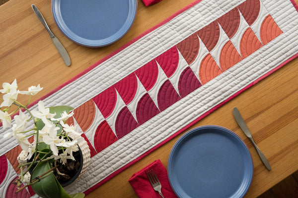 Orchids on table with quilted table runner with Oakshott Fabrics Ruby Red bundle of shot cottons