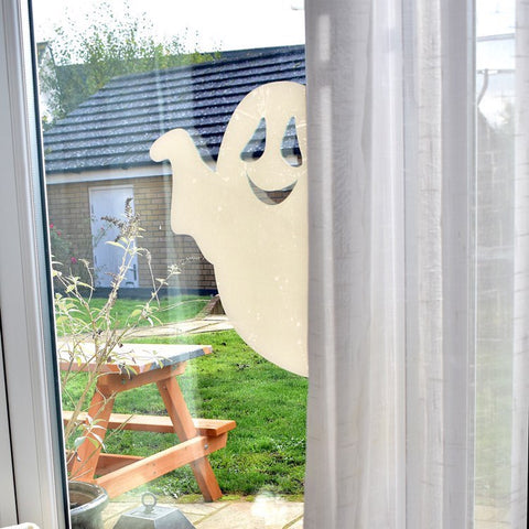 White ghost window sticker peeking out from a curtain in front of a green lawn