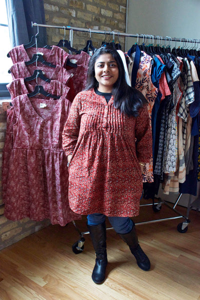 Avani wearing our Vienna Pleated Dress in Red Buds over a black tee, skinny blue jeans, and black tall boots.