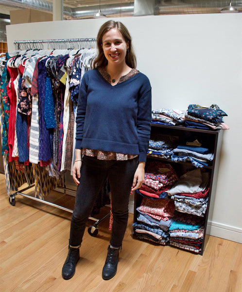 Carly wearing a blue V-neck sweater over the Nomad Pleated Top in Black, black skinny jeans, and black booties.