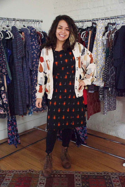 Kayla wearing a cat-patterned cardigan, our Bella Dress in Black/Red Ikat, black tights, and brown boots.