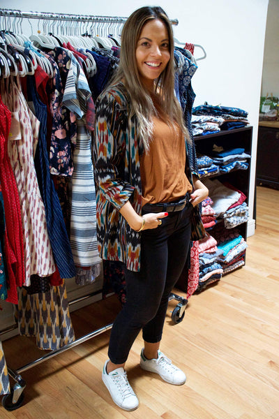 Maya wearing a patterned cardigan, orange tee, black skinny jeans, and white sneakers.